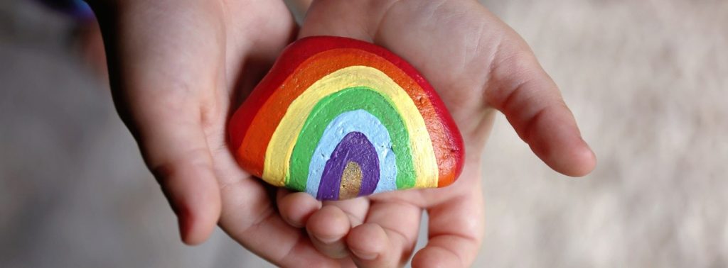 A curved rock painted as a rainbow, being held by a child