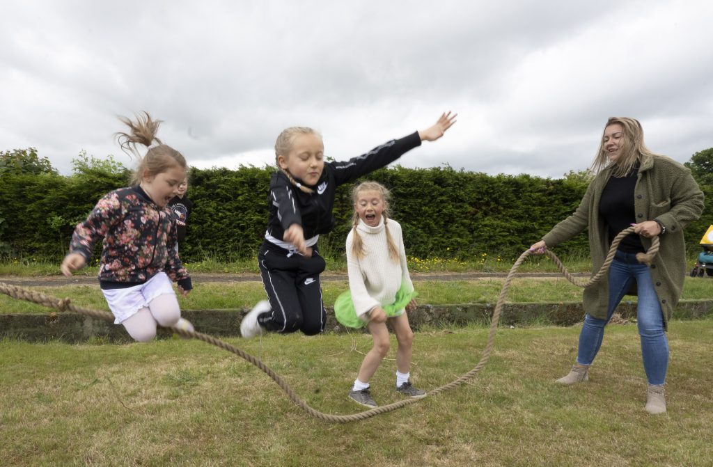 a playworker uses a rope to play skipping with 3 children