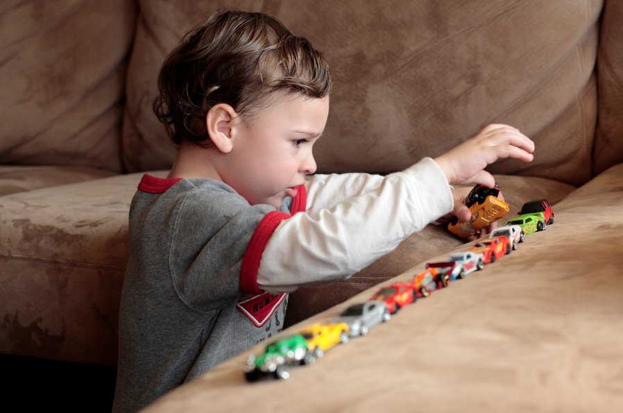 A young boy lining up his toy cars in a row